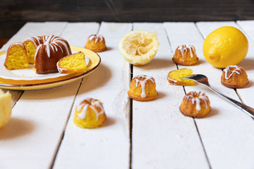 kleiner gelber kuchen bzw gugelhupf aus zitronen mit zuckerguss auf weißem tisch aus brettern und holz