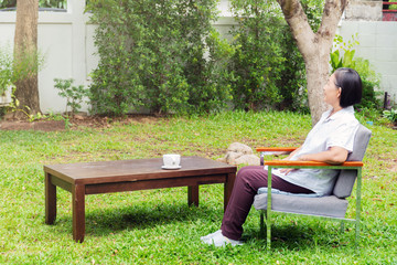 Elderly woman sitting alone in the  front garden and and thinking. Retirement. Senior people lifestyle concept.