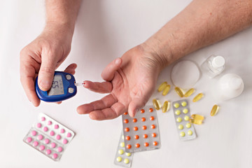 Old hands with sugar meter. Pills and medicines on the table. Old age. Health care for the elderly.
