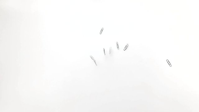 Many paper clips slowly fall onto the table