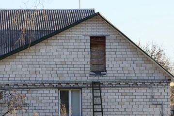 Fototapeta na wymiar white brick loft of a rural house with a window and a door under a gray slate roof against the sky