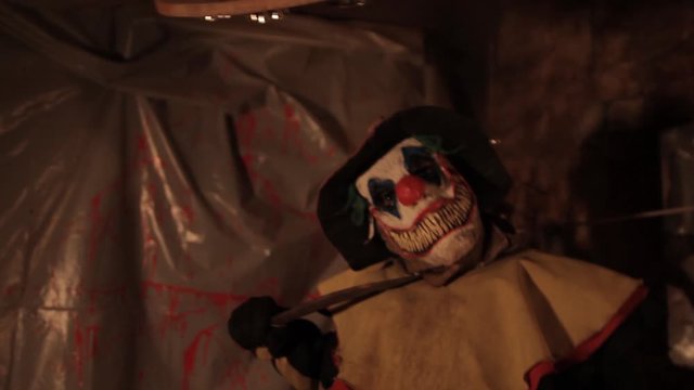 A scarier clown with knife at crude basement with a mirror on the wall