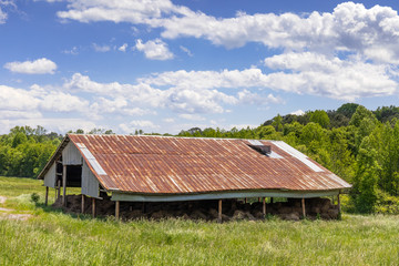 Green meadow with old pole barn, open side filled with hay bales, rusted tin roof, blue sky copy space, horizontal aspect