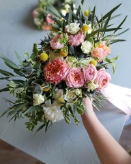 The wedding bouquet lies on the table of the florist in the workshop. This is a disheveled bouquet with long ribbons. Hand holds flowers. This is a photo for a floral lifestyle.