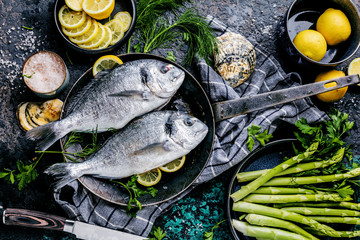 Frischer roher Dorado oder Seebrasse mit Spargel, Gewürzen, Kräutern, Zitrone und Salz auf...
