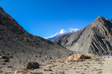A pathway leading through dry Himalayan slopes, in Mustang region, Annapurna Circuit Trek in Nepal. In the back there is snow capped Dhaulagiri I. Barren and steep slopes. Harsh landscape.