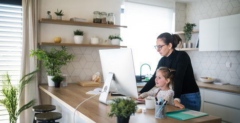 Woman with small daughter working indoors at home office.