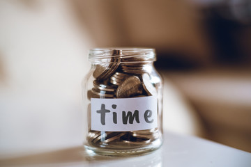 Savings concept for time - Glass jar with coins and inscription.