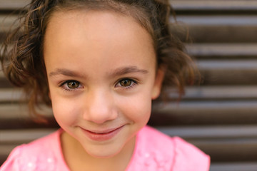 The pretty girl smiles as she looks at the camera. Close-up of a happy little girl