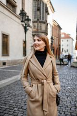 Fototapeta premium Attractive blonde in a beige coat walks around the old town