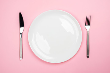 Cutlery on a pink background. Copyspace in the plate. 