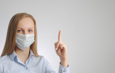 young woman in medical mask points finger up gesture