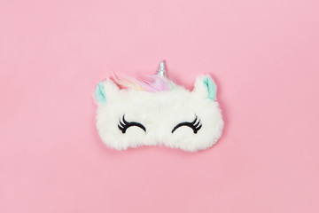 White fluffy fur sleep mask unicorn with closed eyes and small ears on pastel pink paper background, copy space. Top view, flat lay. Concept of vivid dreams. Accessories for girls and young women