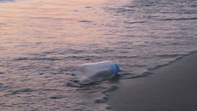 Empty plastic bottle swaying on waves on a sea shore. Plastic pollution. Slow motion. Soft light. Dusk. Golden hour. Summer evening. Ecological concept
