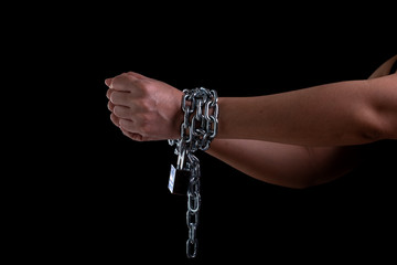 Woman hand tied up with steel chain and lock at the black background, Human rights violations and...