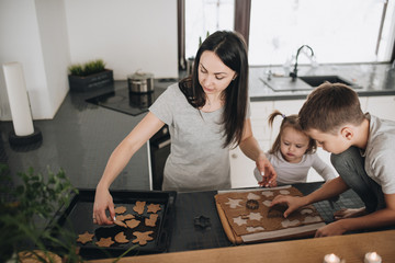 The family prepares gingerbread cookies in the kitchen. Dad, mom, son, daughter, brother and sister. Knead dough, cookie cutters, New Year, Christmas, holiday dinner. Gray homewear.