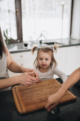 The family prepares gingerbread cookies in the kitchen. Dad, mom, son, daughter, brother and sister. Knead dough, cookie cutters, New Year, Christmas, holiday dinner. Gray homewear.