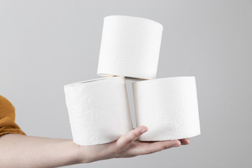 Female hand holds soft toilet rolls on gray background with copy space. Minimal composition for advertisement, article
