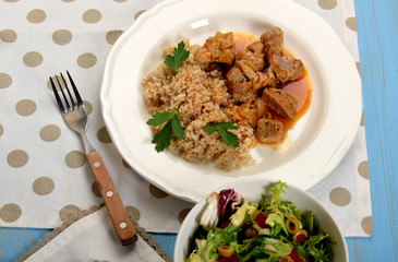 pieces of fried meat with onions and barley on a white plate next to lettuce