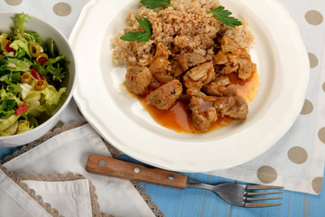 pieces of fried meat with onions and barley on a white plate next to lettuce