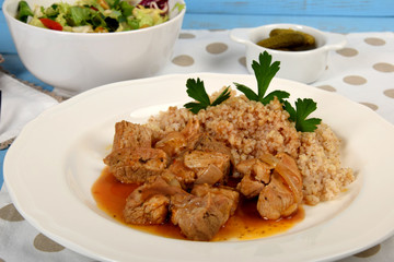 pieces of meat with sauce and barley on a white plate