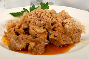 pieces of meat with sauce and barley on a white plate