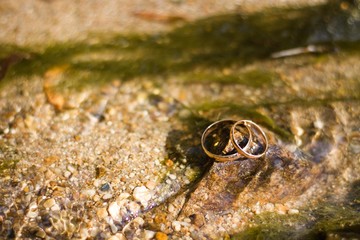 wedding gold rings lie on a stone in a river with running water in the summer