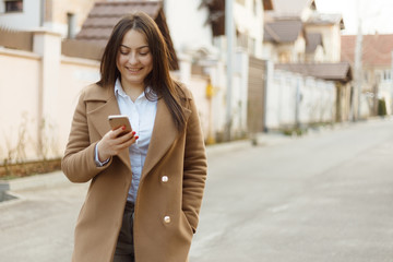 Fototapeta premium Portrait of young beautiful girl outside. Positive young woman spending time outside with her mobile device. Girl with mobile phone.
