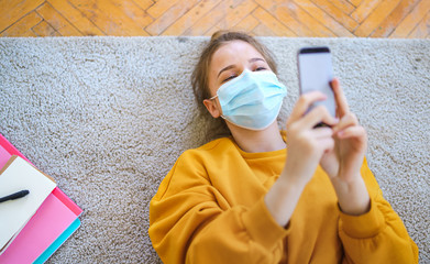 Top view of young girl with smartphone on floor at home, making video call.