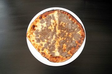 Famous traditional Arabic, Middle East, Israel cuisine. Mutton minced meat Manakeesh on dark wooden background. Lahmeh Bajein Manakish on white plate. Top view 