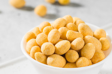 Grilled peanuts in cheese sauce in a white bowl on a light gray table. Close-up with space for text
