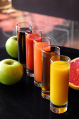 Orange, Apple, tomato, carrot, cherry juice in glass glasses on a black background with apples, grapefruit and mint