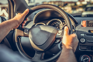 A man drives a car while holding his hands on the steering wheel.