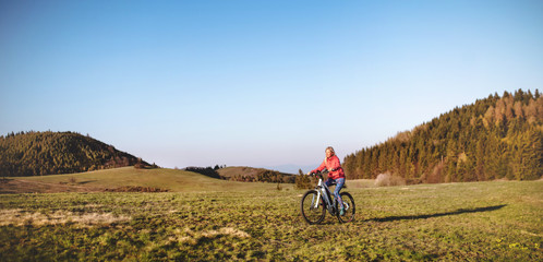 Fototapeta premium Active senior woman with e-bike cycling outdoors in nature.