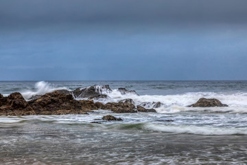 Rocks next to the beach of the Camel Rock bay in New South Wales, Australia at a cloudy and windy day in summer with strong waves in the ocean. 