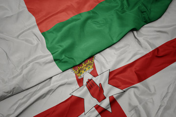 Obraz premium waving colorful flag of northern ireland and national flag of madagascar.