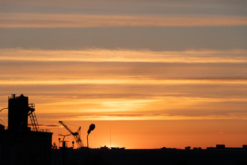 Evening outline of the city. The silhouette of the factory against the sky or sunset. The tower crane operates on the territory of the factory.