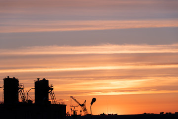 Evening outline of the city. The silhouette of the factory against the sky or sunset. The tower crane operates on the territory of the factory.