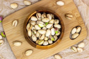 Top view of roasted salted pistachio nuts in nutshell in wooden bowl on textured background.