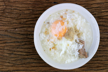 Homemade Thai Rice Soup With chicken, pork and Soft boiled egg or onsen egg in white blow on rustic wooden background. Thai style Food. Top view.