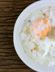 Homemade Thai Rice Soup With chicken, pork and Soft boiled egg or onsen egg in white blow on rustic wooden background. Thai style Food. Top view.