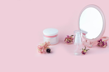 Face care cosmetics. Jars of cream and face serum and a mirror on a pink background. Home Skin Care Concept