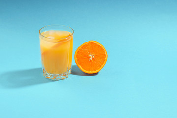 A glass of orange juice and half cut orange on a light blue background. Freshly squeezed orange juice.
