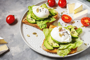 Healthy sandwich - poached eggs and avocado on toast with tomatoes on concrete background.
