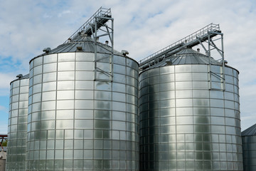 silver silos on agro manufacturing plant for processing drying cleaning and storage of agricultural products, flour, cereals and grain. Large iron barrels of grain. Granary elevator