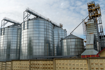 silver silos on agro manufacturing plant for processing drying cleaning and storage of agricultural products, flour, cereals and grain. Large iron barrels of grain. Granary elevator