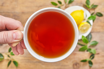 Hand holding cup of tea with lemon on wooden background. Top view.