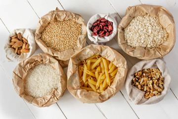 Groats, pasta, nuts, and dried fruits in paper and cotton bags on white wooden table. Top view. Zero waste, eco friendly or plastic free lifestyle concept. 