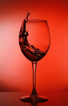 Splash of wine in the glass. silhouette of wine glass on red background. studio shot. a glass of alcohol