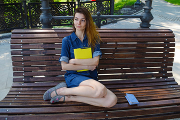 A young girl sits on a bench with a book in her hands